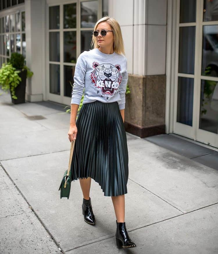 Mujer que lleva una sudadera gris con una falda plisada y botines